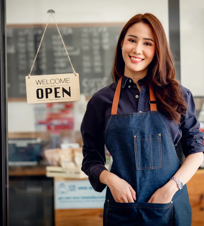 Cafe owner in a denim apron standing beside the open sign at her shop entrance